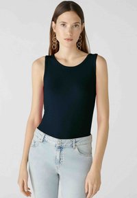 Black ribbed tank top with a round neckline, paired with light blue distressed jeans. Notable details include medium-width shoulder straps.