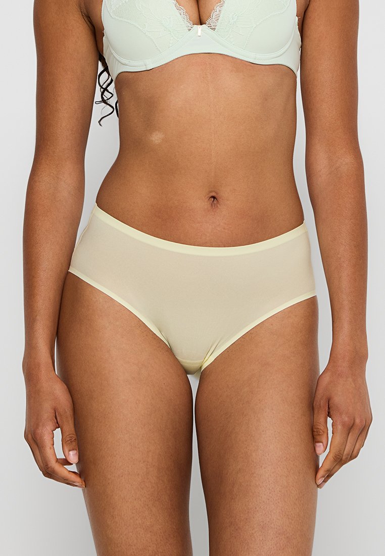 Pale gele damesondergoed met een gladde, rekbare textuur en een contrasterende lichtgele rand bij de taille en beenopeningen.