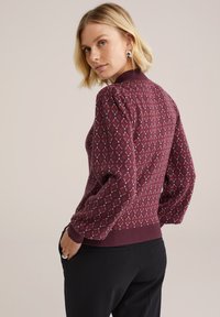 Bordeaux-gepatroneerd sweater met diamanten motieven, geribbelde manchetten en een getailleerde pasvorm. Zachte textuur, met poefmouwen voor extra diepte.