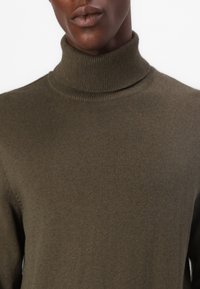 Olivno zelena turtleneck pulover iz fine pletenine, z odebeljenim detajlom na ovratniku in gladko teksturo.