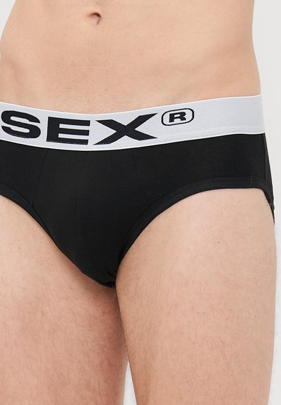Männlicher Oberkörper, der schwarze Unterhosen mit einem weißen Bund trägt, auf dem fett gedruckte schwarze Schrift und ein eingetragenes Markenzeichen zu sehen sind.