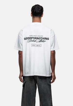 T-shirt oversize bianca in cotone con testo nero sul retro che recita "GOODFORNOTHING British Atelier" e "NORTH WEST, ENGLAND."