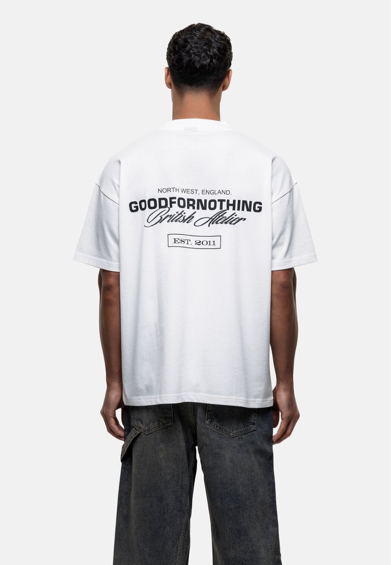 T-shirt oversize en coton blanc avec du texte noir au dos indiquant "GOODFORNOTHING British Atelier" et "NORTH WEST, ENGLAND."