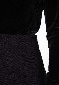 Černý sametový top s dlouhými rukávy spárovaný s černými vysokým pasem úpletovými kalhotami s texturou a žebrovaným vzorem.