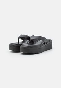 Mustat alustossut, joissa on kumipohja ja sileä nahkaremmi. Varustettu thong-designilla ja vähäisellä tekstuurilla pohjassa pitämään otteesta kiinni.