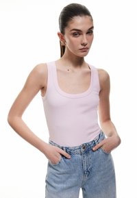 Vaaleanpunainen ribbipinta tanktoppi, jossa on pyöreä pääntie, yhdistettynä korkeavyötäröisiin vaaleansinisiin farkkuihin. Minimalistinen muotoilu, istuva silhuetti.