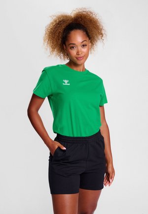 Grøn bomulds t-shirt med et lille hvidt logo, parret med sorte shorts med elastisk talje. Begge genstande har et afslappet design og blød tekstur.