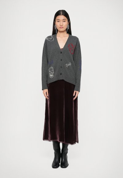 Cardigan grigio lavorato a maglia con chiusura a bottoni, caratterizzato da disegni ricamati. Accompagnato da un vestito lungo in velluto borgogna e stivali neri alla caviglia.