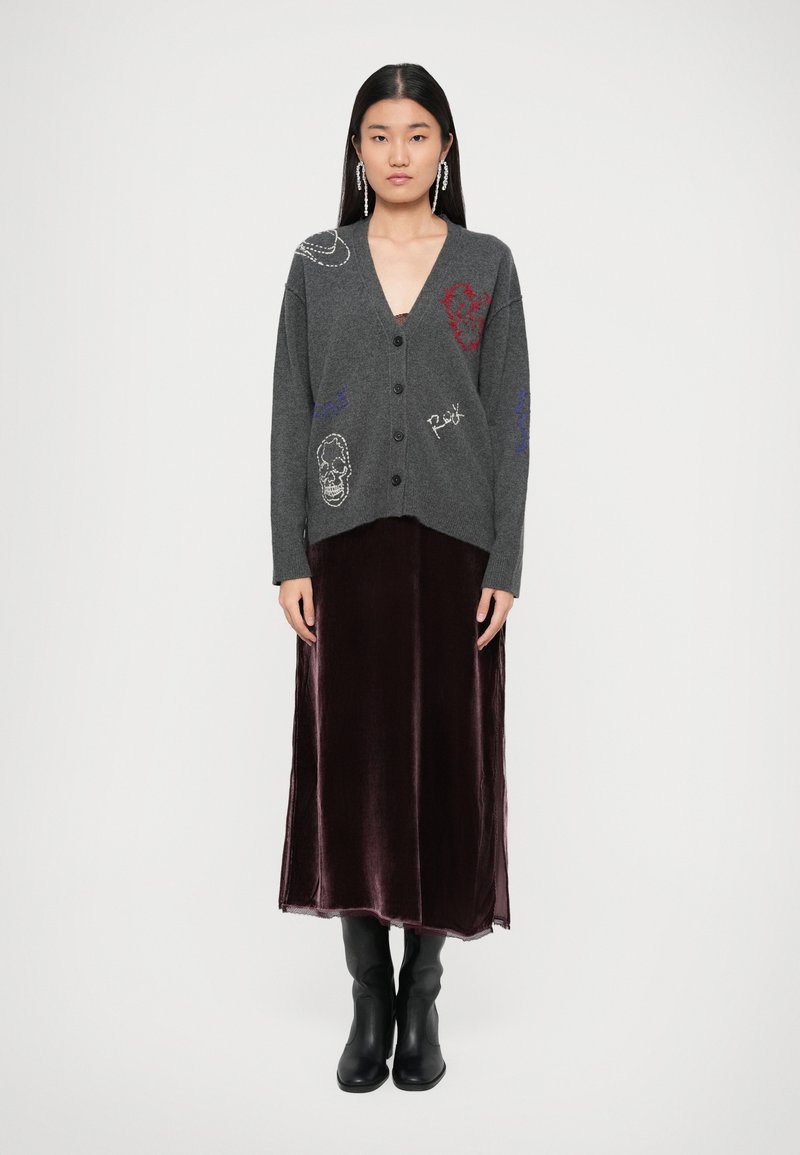 Grijze gebreide cardigan met knopen aan de voorkant, voorzien van geborduurde ontwerpen. Gemoedelijk gedragen met een bordeauxvelours maxi-jurk en zwarte enkellaarsjes.