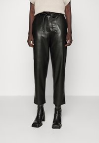 Svarta läderbyxor med hög midja, dragsko-bälte, framstygn och lös passform, som är kombinerade med svarta klackade ankelstövlar.