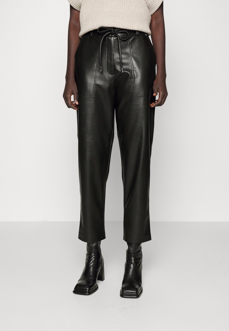 Svarta läderbyxor med hög midja, dragsko-bälte, framstygn och lös passform, som är kombinerade med svarta klackade ankelstövlar.