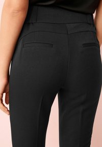 Schwarze maßgeschneiderte Hosen mit glatter Textur, schmaler Passform und zwei Gesäßtaschen mit eleganten Nähdetails.