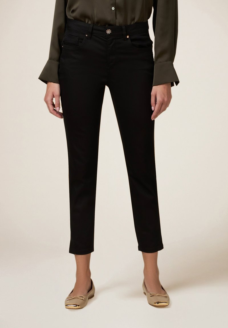 Zwarte slim-fit broek van een gladde stof, met voorzakken, een knoopsluiting en decoratieve stiksels, gecombineerd met gouden flats.
