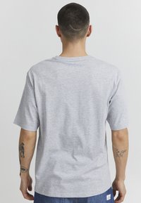 Gray short-sleeve t-shirt made of cotton with a crew neck. Features a simple design and relaxed fit, viewed from the back with visible tattoos.