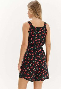 Černý overal s potiskem třešní, s čtvercovým zadním dílem, širokými ramínky a elastickým pasem pro uvolněný střih. Měkká, lehká tkanina.