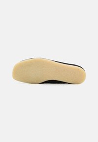 Sola di scarpa nera con superficie texture e bordi arrotondati, dotata di uno strato inferiore in gomma color crema per aderenza e durata.