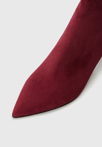 Bottines bordeaux en daim à bout pointu avec un design élancé, présentant une texture lisse et une silhouette mince s'étendant juste au-dessus de la cheville.