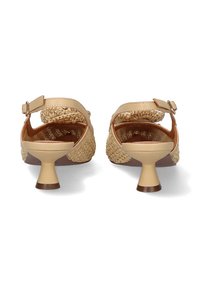 Sandalias beige con una parte superior de paja trenzada, correa ajustable en el tobillo y tacón bajo en forma de campana. Textura suave y plantilla marrón visible.