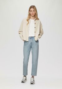 Beżowa koszula z guzikami, biała podkoszulka, jasnoniebieskie dżinsy o prostym kroju oraz srebrne trampki. Gładkie tekstury, luźny krój, minimalistyczny design.