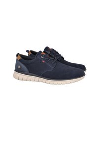 Zapatos de ante azul marino con suela beige clara, diseño de cordones y detalles en cuero marrón. Presentan un pequeño logotipo en el lateral.