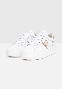 Sneakers bianchi con finitura lucida, occhielli dorati e un accento a forma di cuore. Presentano una spessa suola platform bianca e un design con lacci.