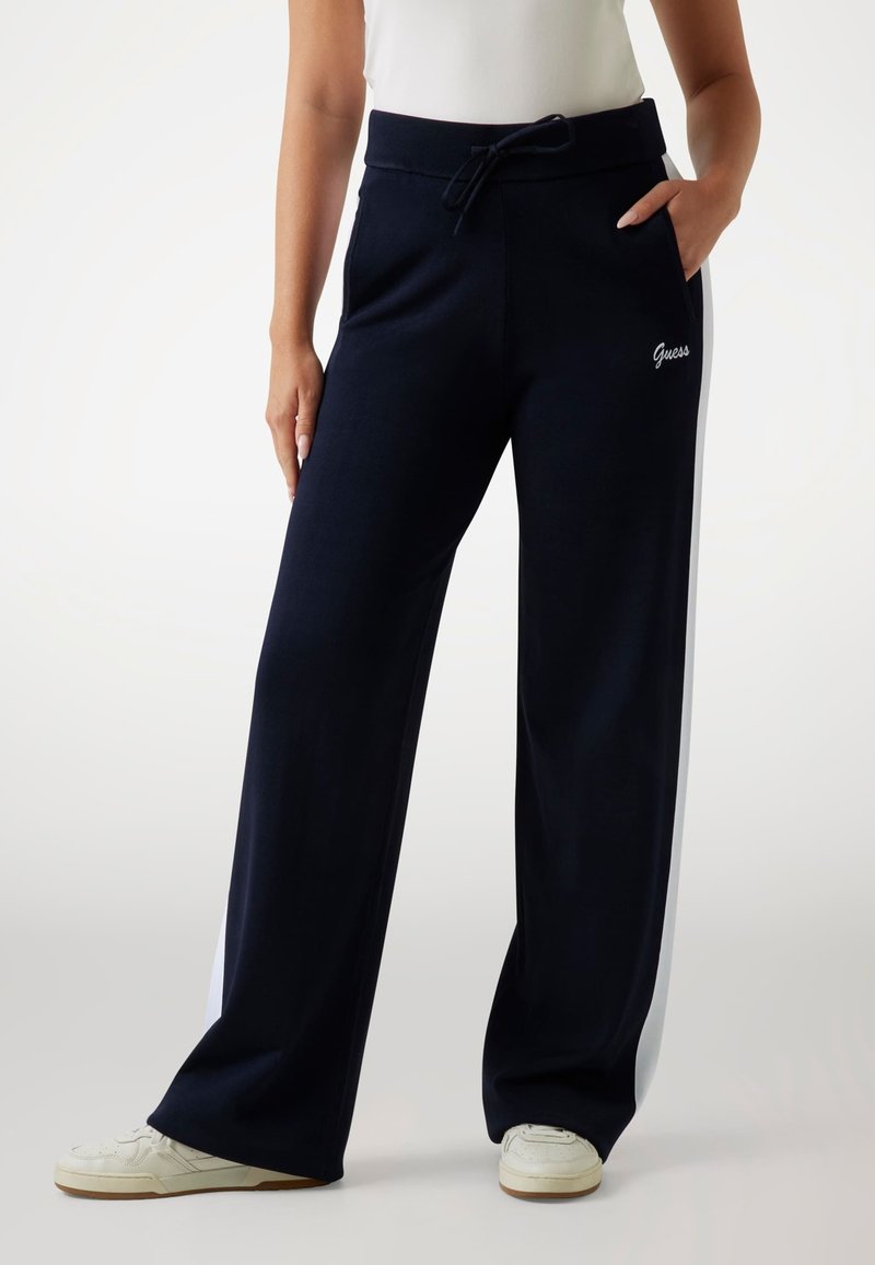 Marineblauwe sweatpants met witte zijstrepen, elastische tailleband met trekkoord, voorzien van een frontzak en het "Guess"-logo in witte borduring.