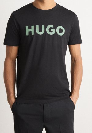 Czarny bawełniany T-shirt z dużym zielonym logo "HUGO" na piersi. Krótkie rękawy i klasyczny okrągły dekolt. Gładka tekstura.