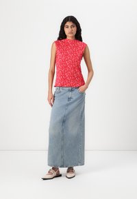 Rød blomstret ermeløs topp med en samlet tekstur, parret med en lyseblå denimmaxiskjørt og beige flate sko med stropper.