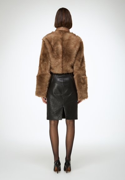 Veste en fausse fourrure marron à manches larges, associée à une jupe crayon en cuir noir dotée d'une fente arrière et de surpiqûres ton sur ton. Des talons noirs complètent le look.