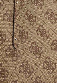 Tela marrón con patrón de diseño geométrico que presenta motivos en relieve. El material parece texturizado, complementado por un borde negro y un broche de metal.