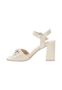 Sandalo con tacco alto in pelle sintetica beige, con punta aperta, cinturino alla caviglia e dettagli decorativi in argento frontalmente, design con tacco a blocco.