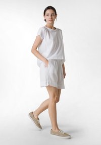 Vit kortärmad topp och matchande shorts, tillverkade av lätt tyg. Avslappnade beige sneakers fullbordar outfiten. Enkelt mönster med fickor.