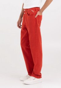 Pantaloni di cotone rossi con una vestibilità ampia, design a cinque tasche, accessori in contrasto e una texture liscia. Abbinati a sneakers bianche.