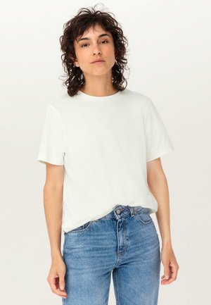 Weißes Baumwoll-T-Shirt mit rundem Halsausschnitt und kurzen Ärmeln, kombiniert mit blauen Jeans. Einfaches Design, glatte Textur, keine sichtbaren Muster.