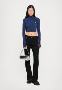 Cropped turtleneck top in blue with abstract pattern, paired with black flared pants and a silver metallic handbag. Chunky black shoes.