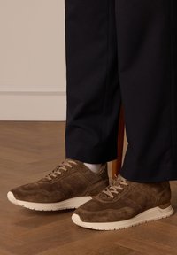 Bruine suède sneakers met textuurpanelen, crème rubberen zool en beige veters. Draagt bij donkere broeken, tentoongesteld op een houten vloer.