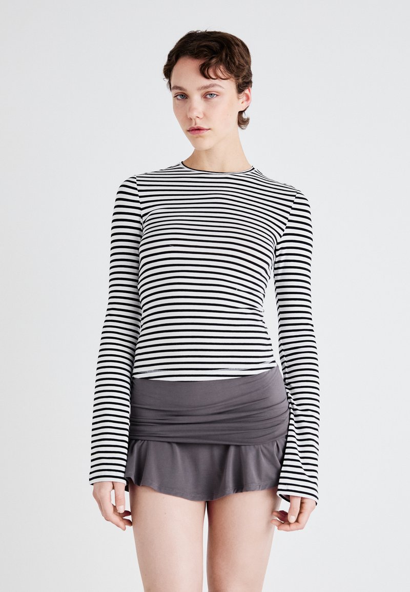 Striped long-sleeve top in black and white, paired with a fitted gray skirt featuring a flared hem. Soft fabric with a smooth texture.