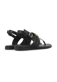 Sandalias de cuero negro con correas ajustables en el tobillo, acentos de hebilla dorada, suelas planas y un diseño tipo entrepierna. Detalle texturizado en las correas.