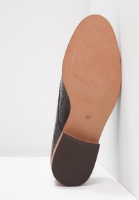 Suola di scarpa in pelle intrecciata nera con fondo in gomma liscia color cammello; presenta un'indicazione della taglia 37 e linee di presa testurizzate.