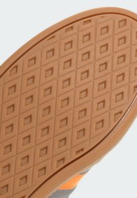 Podošva gumovej topánky s mriežkovým vzorom štvorcov a diamantov, s hladkým hnedým povrchom a akcentmi v oranžovej a sivej farbe.