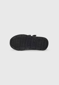 Semelle de chaussure en caoutchouc noir avec des motifs de grip texturés, comportant un design segmenté et des perforations pour le drainage. Marque visible sur le côté.