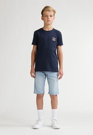 Marineblauw katoenen T-shirt met een klein logo op de borst, gecombineerd met lichtblauwe denim shorts en witte sokken met witte sneakers.