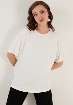 Bluză albă cu mânecă scurtă, decolteu rotund, croială lejeră și textură moale, asortată cu pantaloni negri pentru un contrast.