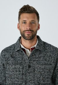 Šedý kabát s kockovaným vzorom, ktorý má zapínanie na gombíky, golier a textúrovanú látku. Nosí sa cez bielu a vínovú košeľu.