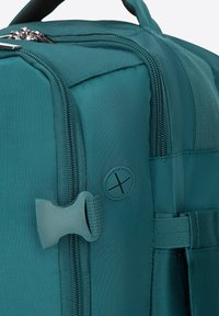 Turkusowy plecak podróżny z teksturowanej tkaniny, podwójnymi suwakami, boczną klamrą i okrągłym logo. Solidny uchwyt do noszenia.