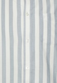 Camicia leggera con bottoni, caratterizzata da righe verticali blu e bianche. Il tessuto presenta una finitura liscia, con una tasca sul petto e bottoni perla.