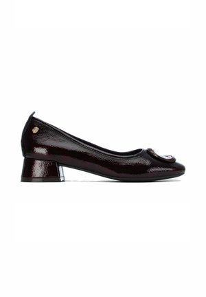 Zapato de mujer de tacón bajo, de color marrón oscuro brillante, con punta redondeada y detalle decorativo de hebilla en la parte superior, mostrado de perfil lateral sobre fondo blanco.