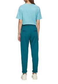 Turkusowe dresy z elastycznym pasem i dwoma tylnymi kieszeniami, w zestawie z jasnoniebieską koszulką z krótkim rękawem. Widać białe trampki.