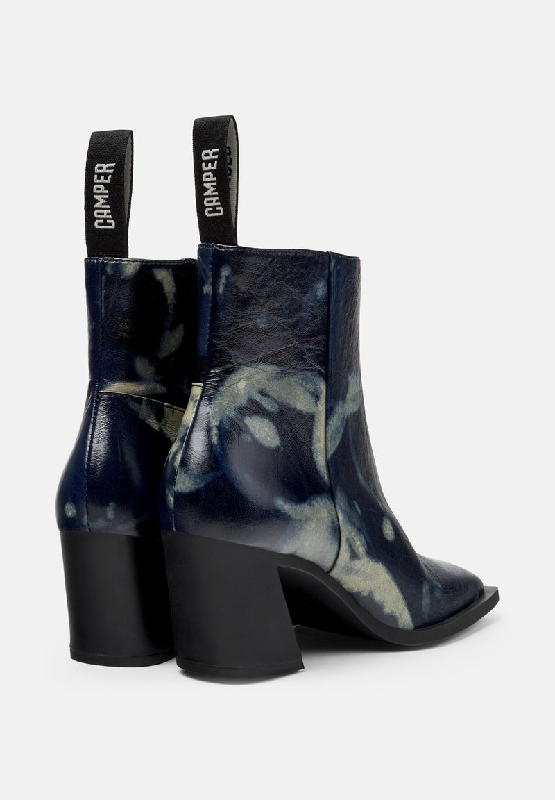 Ankelstövlar i marinblått läder med ett marmormönster, svart blockklack och en dragflik med varumärket. Slät textur.