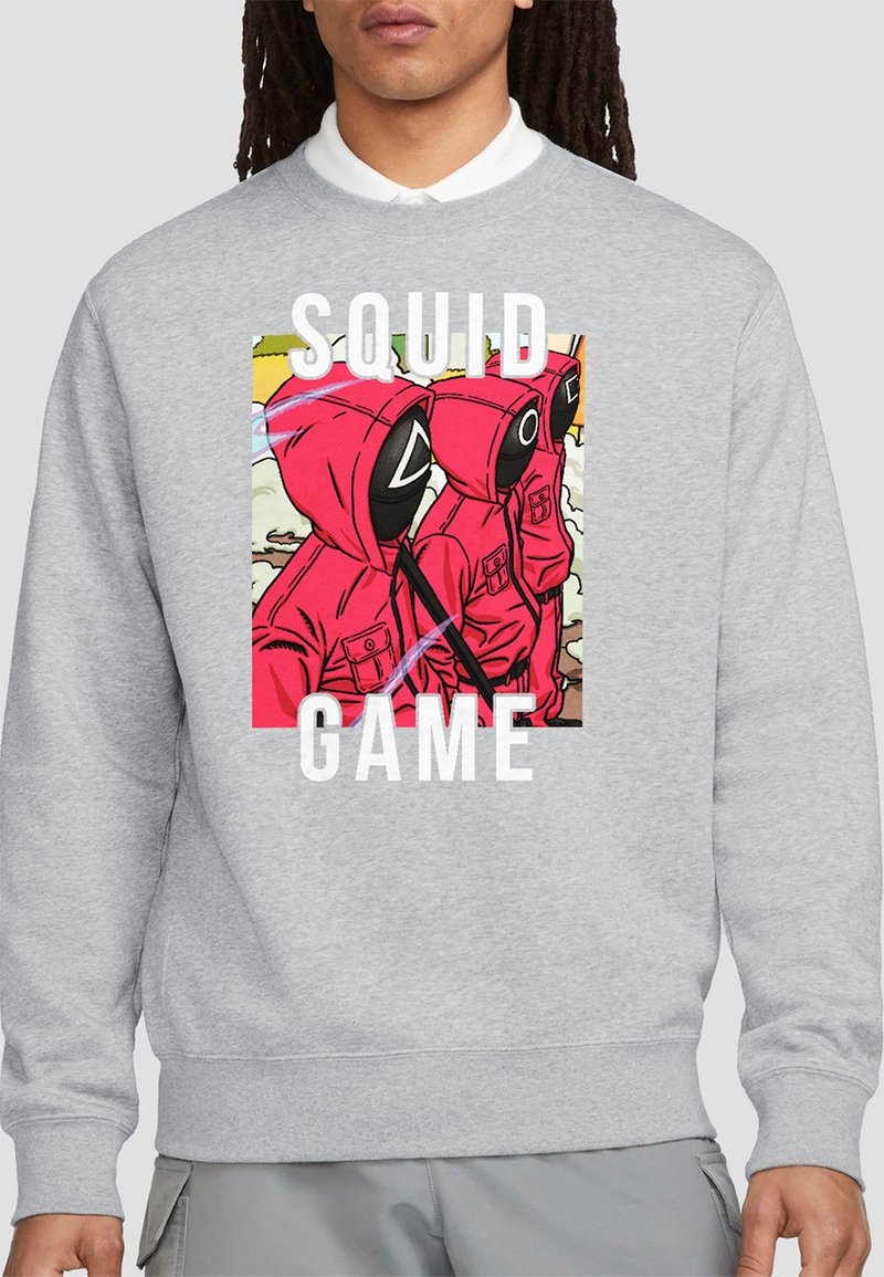 Gray sweatshirt with a colorful print featuring red hooded figures with masks, bold white text reading "SQUID GAME." Standard crewneck style.